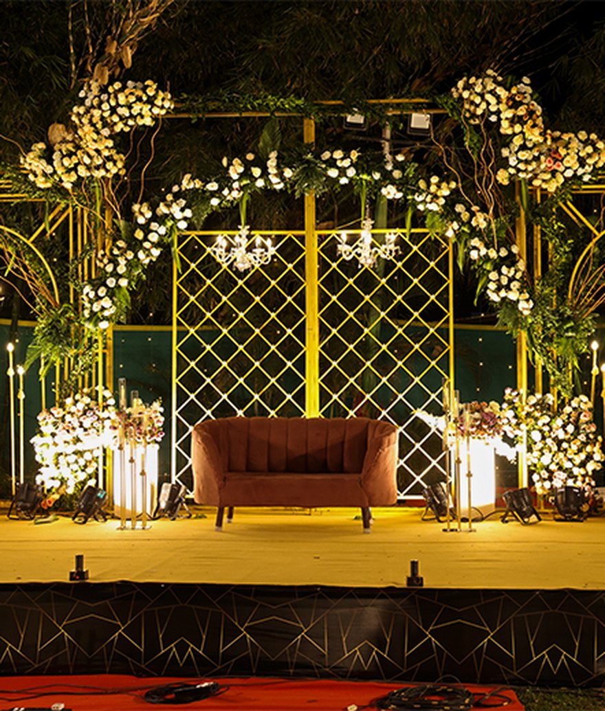 Bespoke floral-arch stage with lounge seating and warm lighting by Versato Ventures, Bengaluru